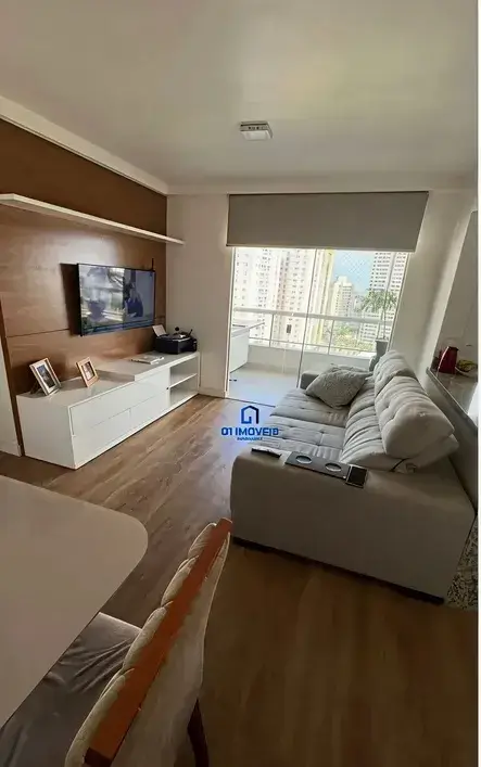 Sala de estar com sofá cinza, rack branco e painel amadeirado no Condomínio Residencial You.