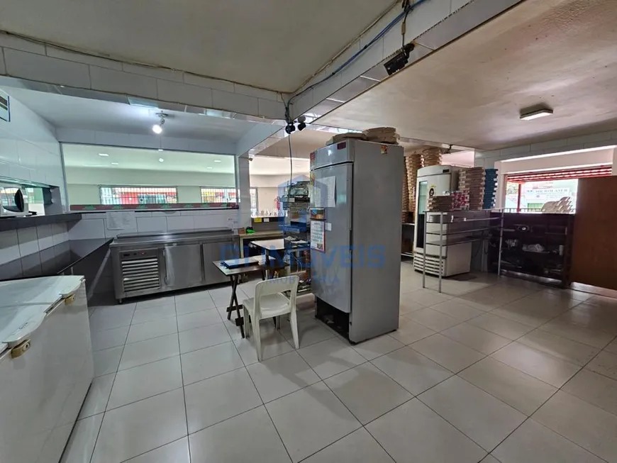 Cozinha industrial da pizzaria com prateleiras de inox, caixas de pizza empilhadas e piso branco.