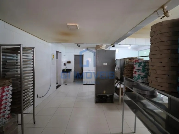 Área externa coberta da pizzaria com telhado aparente, grade de proteção e cadeiras armazenadas.