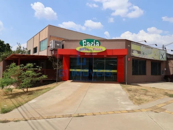 Vista lateral da pizzaria mostrando a entrada principal vermelha, calçada ampla e estacionamento.