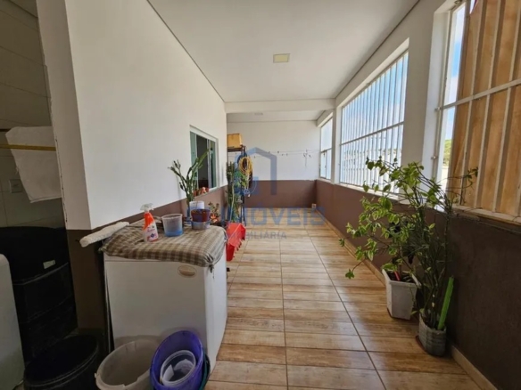 Área de serviço em varanda longa com máquina de lavar, piso cerâmico amadeirado e plantas.