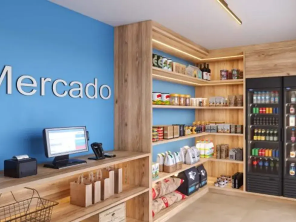 Minimercado de conveniência dentro do condomínio com prateleiras de alimentos e geladeiras de bebidas self-service.
