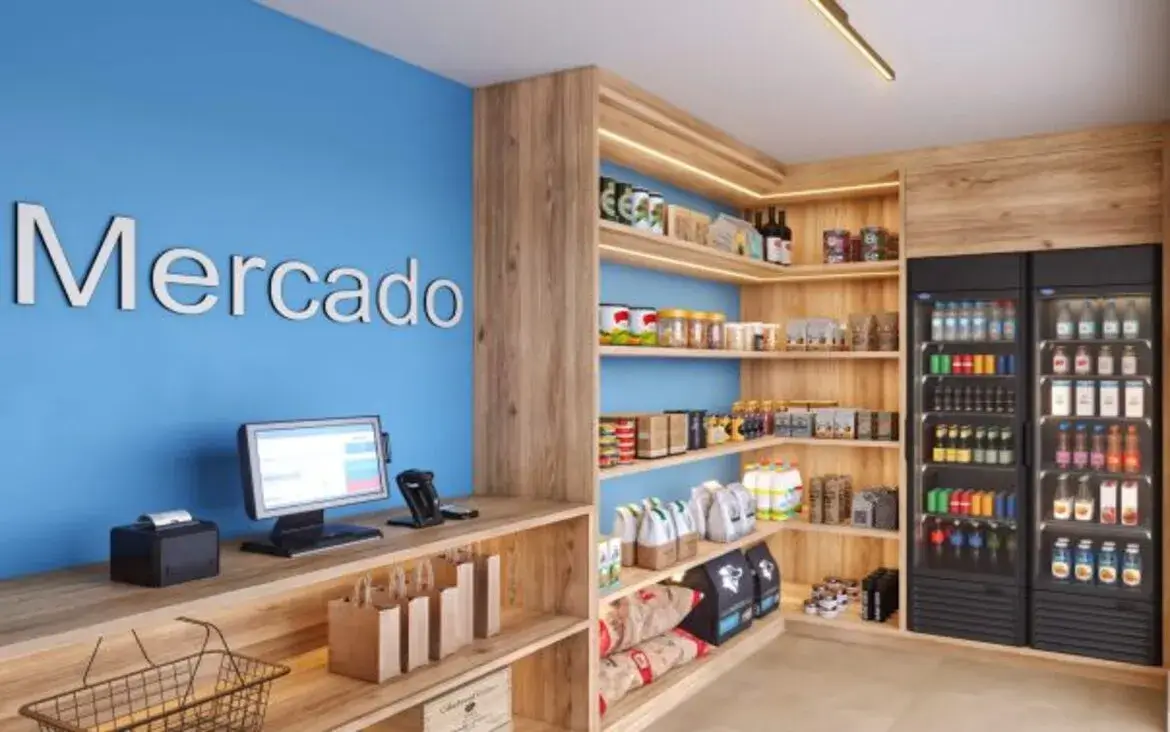 Minimercado de conveniência dentro do condomínio com prateleiras de alimentos e geladeiras de bebidas self-service.