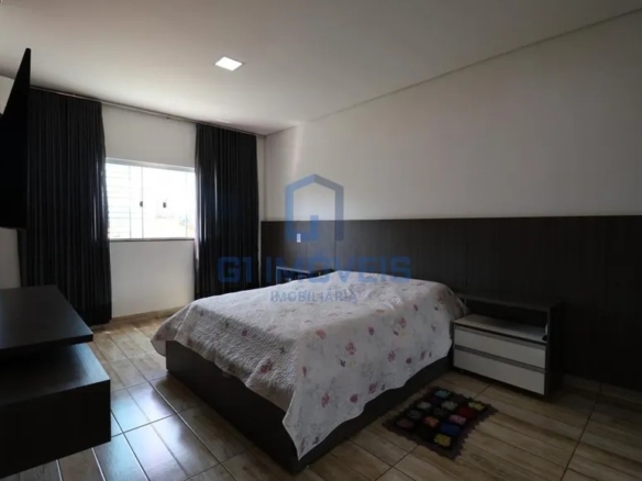 Quarto de casal espaçoso com cama box, cortinas escuras do teto ao chão e piso amadeirado.