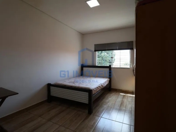 Quarto de solteiro simples com cama de madeira escura, guarda-roupa e janela com grade.