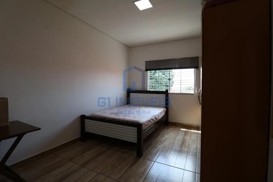 Quarto de solteiro simples com cama de madeira escura, guarda-roupa e janela com grade.