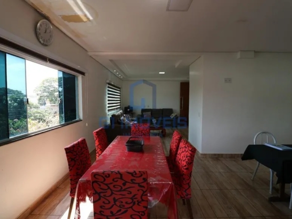 Sala de jantar ampla com mesa retangular, cadeiras vermelhas e grande janela de vidro com vista.