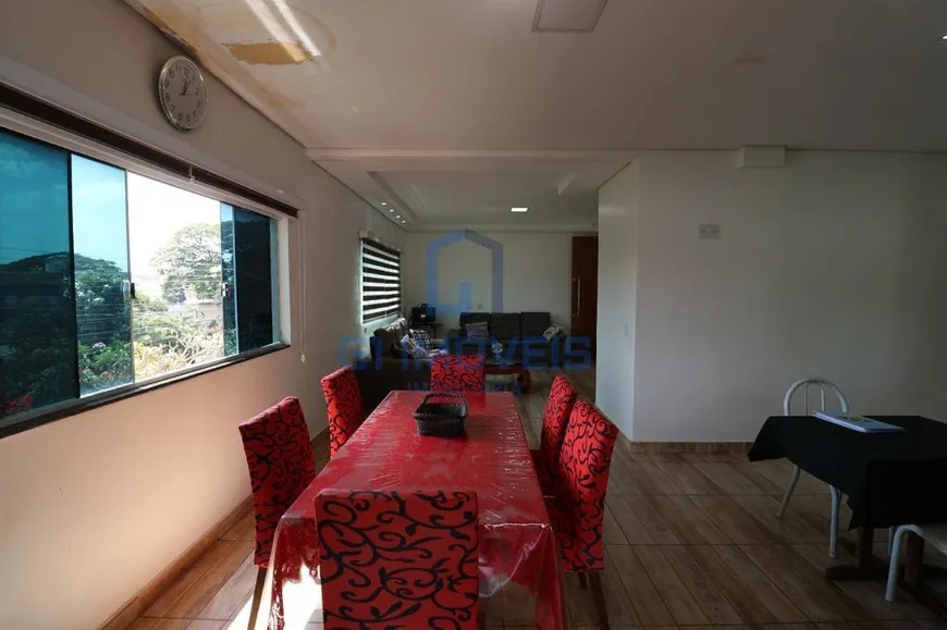 Sala de jantar ampla com mesa retangular, cadeiras vermelhas e grande janela de vidro com vista.
