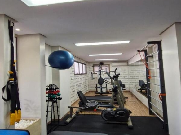 Espaço fitness do condomínio com esteiras, pesos, bancos de supino e equipamentos de musculação.
