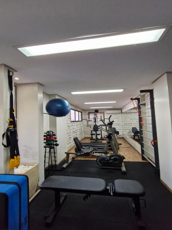 academia-condominio-equipamentos-completos Espaço fitness do condomínio com esteiras, pesos, bancos de supino e equipamentos de musculação.