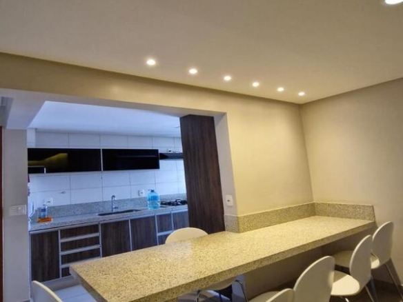 Bancada de refeições em granito com sete cadeiras brancas modernas em ambiente iluminado.