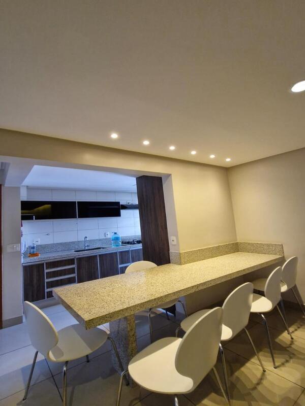 bancada-gourmet-granito-cadeiras-brancas Bancada de refeições em granito com sete cadeiras brancas modernas em ambiente iluminado.