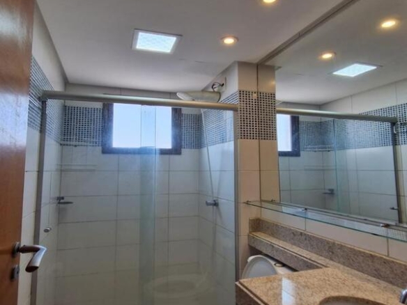 Banheiro social com bancada de mármore bege, box de vidro e acabamento em pastilhas azuis.