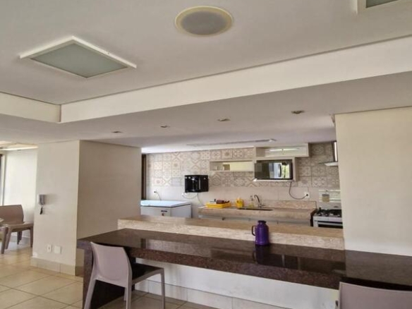 Área de refeições com bancada escura e cadeiras brancas de design moderno integradas à cozinha.