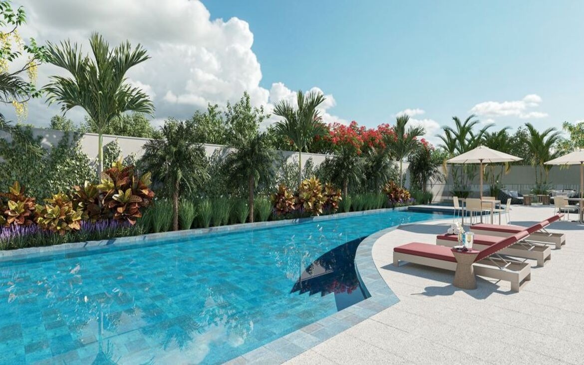 Piscina adulta ao ar livre no condomínio Dot Bild, cercada por espreguiçadeiras e vegetação tropical.