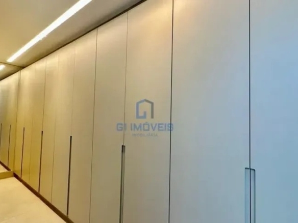 Closet planejado amplo com armários brancos e iluminação linear no teto.