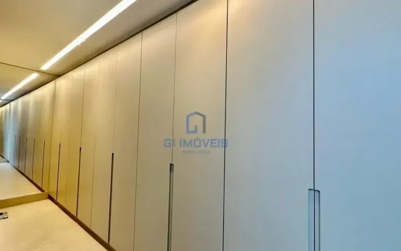 Closet planejado amplo com armários brancos e iluminação linear no teto.