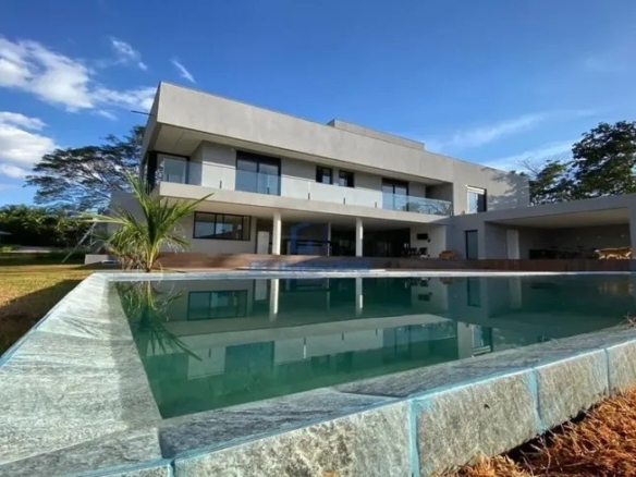 Fachada de casa moderna de luxo com piscina e deck de pedra sob céu azul.