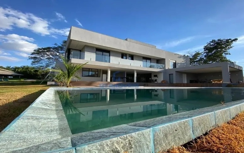Fachada de casa moderna de luxo com piscina e deck de pedra sob céu azul.