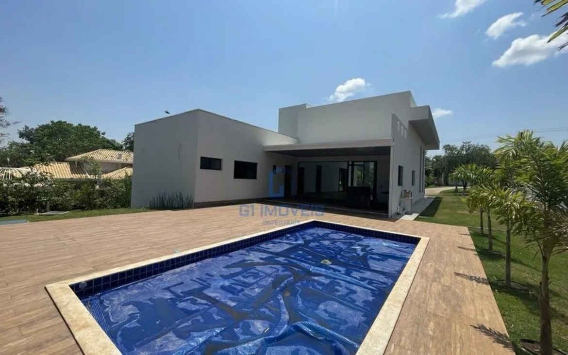 Piscina privativa revestida em pastilhas azuis com amplo deck de madeira e projeto paisagístico ao fundo.