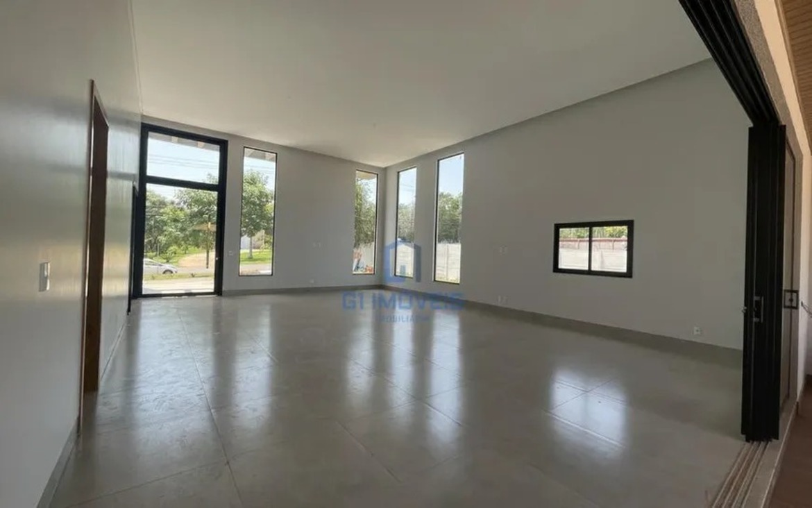 Sala de estar com pé-direito elevado e grandes aberturas de vidro para máxima iluminação natural.