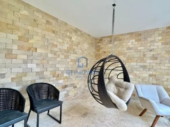 Varanda gourmet com balanço suspenso e parede de pedras naturais no Aldeia do Vale.