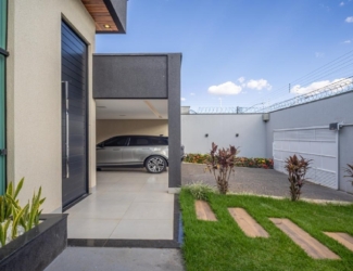 Corredor externo da residência com gramado e acesso à garagem