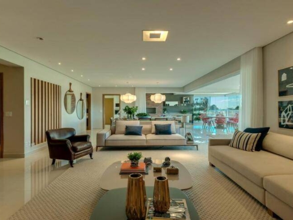 Sala de estar com sofá e mesa, além de iluminação embutida e revestimento claro
