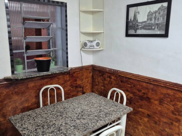 Sala de estar com mesa, cadeiras e painel de televisão, além de iluminação embutida e revestimento claro