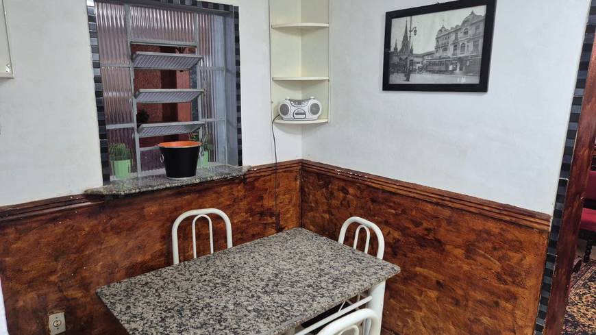 Sala de estar com mesa, cadeiras e painel de televisão, além de iluminação embutida e revestimento claro
