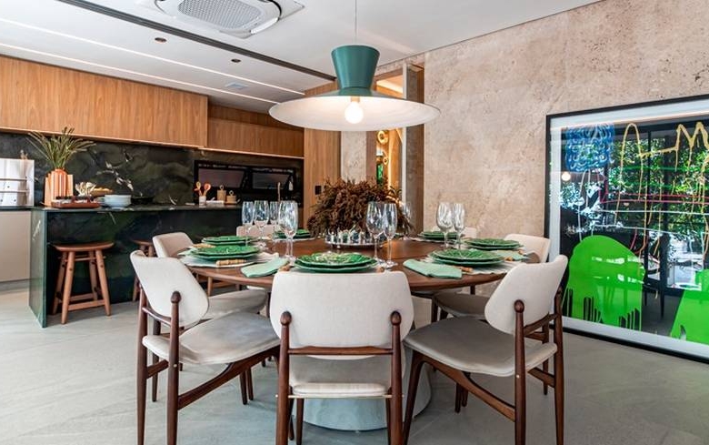 Sala de estar com mesa, cadeiras e painel de televisão, além de iluminação embutida e revestimento claro