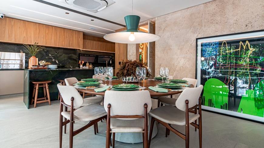 Sala de estar com mesa, cadeiras e painel de televisão, além de iluminação embutida e revestimento claro