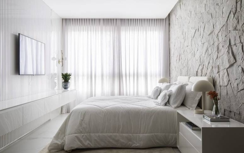 Quarto com cama e painel de televisão, além de iluminação embutida e revestimento de madeira