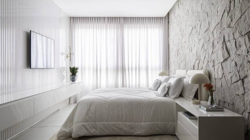 Quarto com cama e painel de televisão, além de iluminação embutida e revestimento de madeira