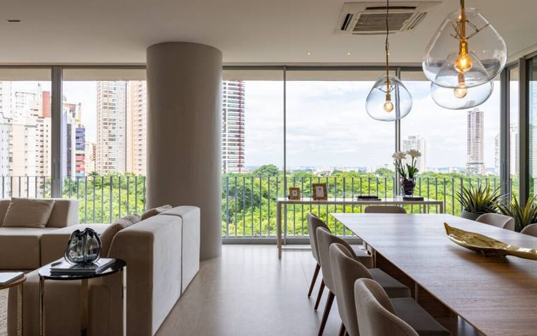 Sala de estar com sofá e mesa, além de iluminação embutida e revestimento claro