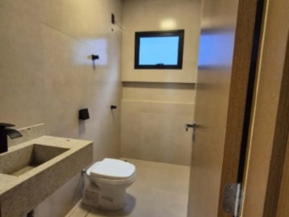Banheiro moderno com bancada, vaso sanitário, box de vidro e janela em casa no Alto Umuarama, Uberlândia, Minas Gerais.