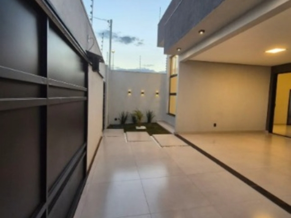 Corredor externo com piso claro, portão preto e área coberta em casa no Alto Umuarama, em Uberlândia, Minas Gerais.