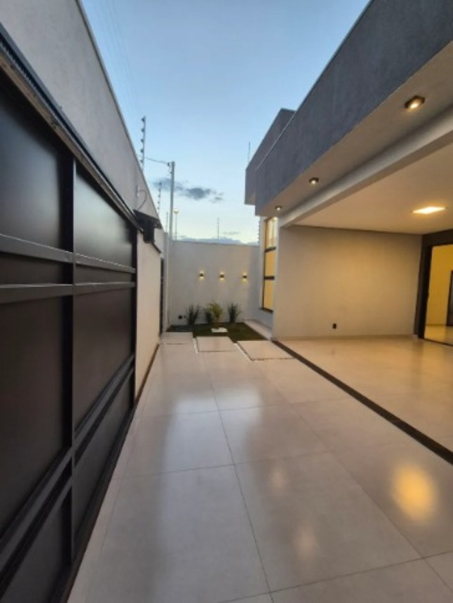Corredor externo com piso claro, portão preto e área coberta em casa no Alto Umuarama, em Uberlândia, Minas Gerais.