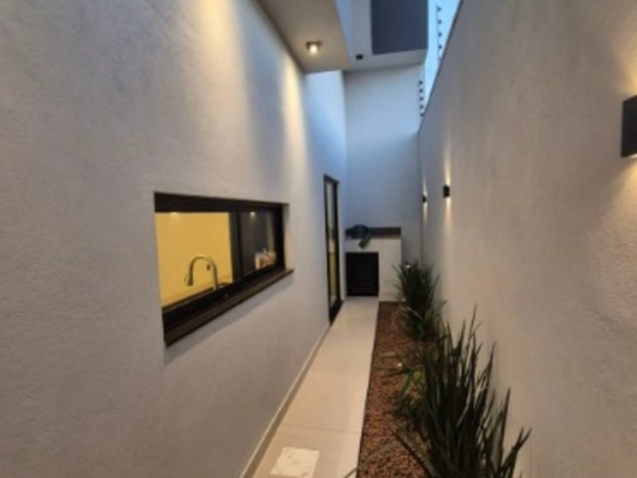 Corredor lateral iluminado com jardim e janela em casa moderna no bairro Alto Umuarama, em Uberlândia, Minas Gerais.