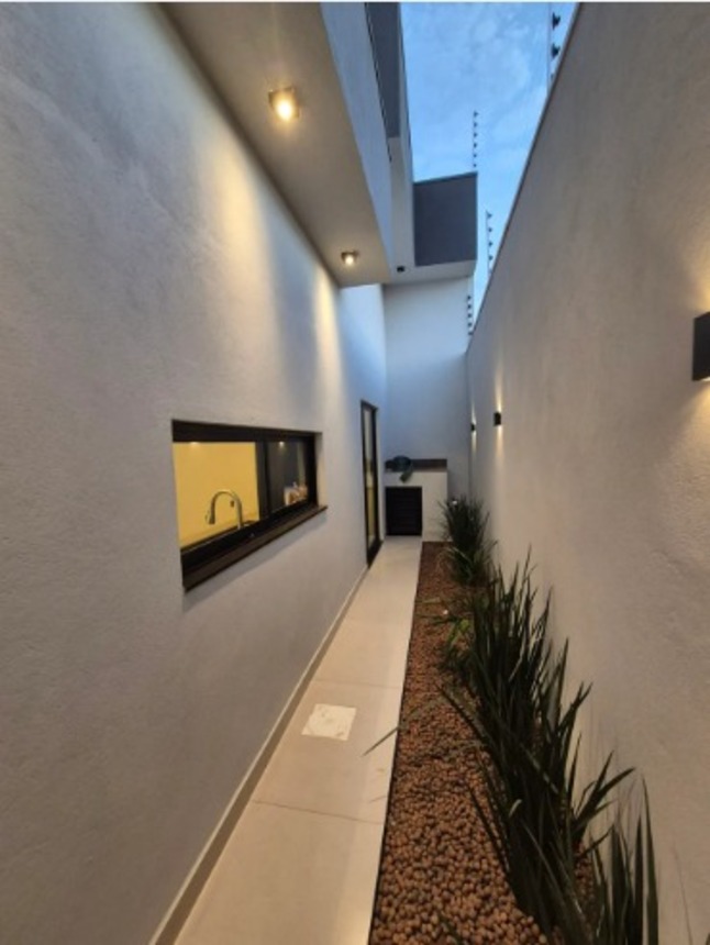 Corredor lateral iluminado com jardim e janela em casa moderna no bairro Alto Umuarama, em Uberlândia, Minas Gerais.