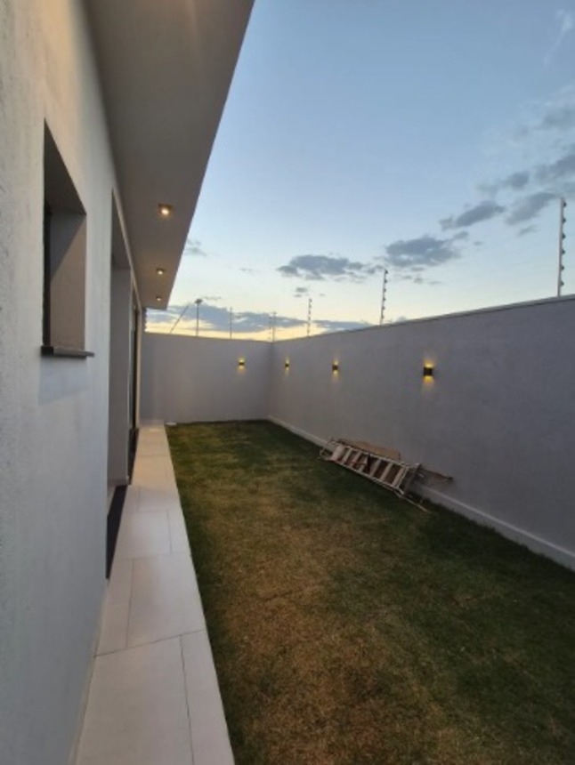 Quintal com gramado, muro alto e corredor lateral de casa no bairro Alto Umuarama, em Uberlândia, Minas Gerais.