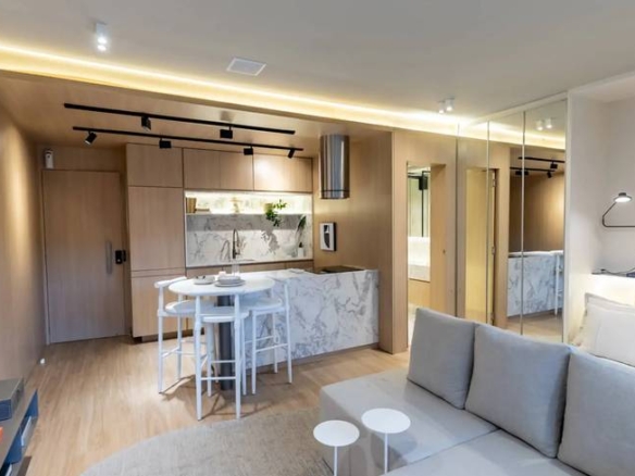 Sala de estar com sofá e mesa, além de iluminação embutida e revestimento claro