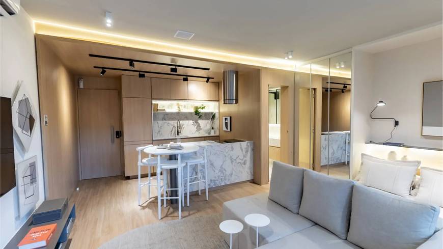 Sala de estar com sofá e mesa, além de iluminação embutida e revestimento claro