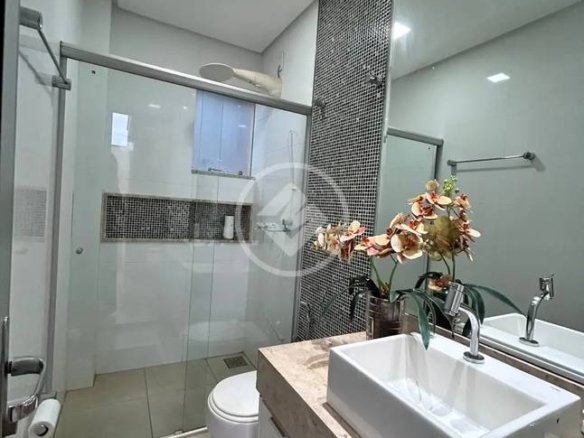 Banheiro com pia, lavatório e espelho, além de iluminação embutida e revestimento de madeira no Alphaville Araguaia