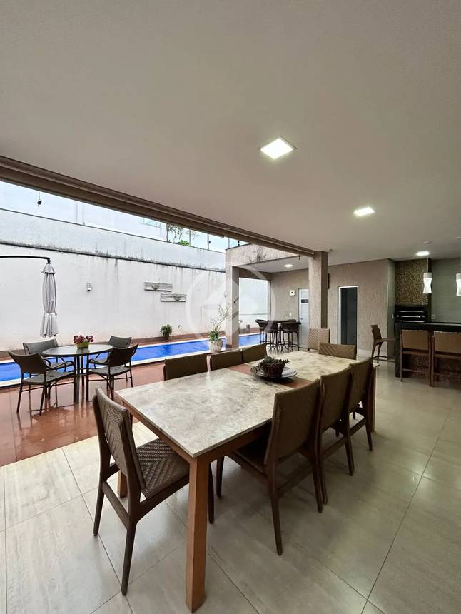 Sala de estar com mesa, cadeiras e luminária, além de iluminação embutida e piso de madeira