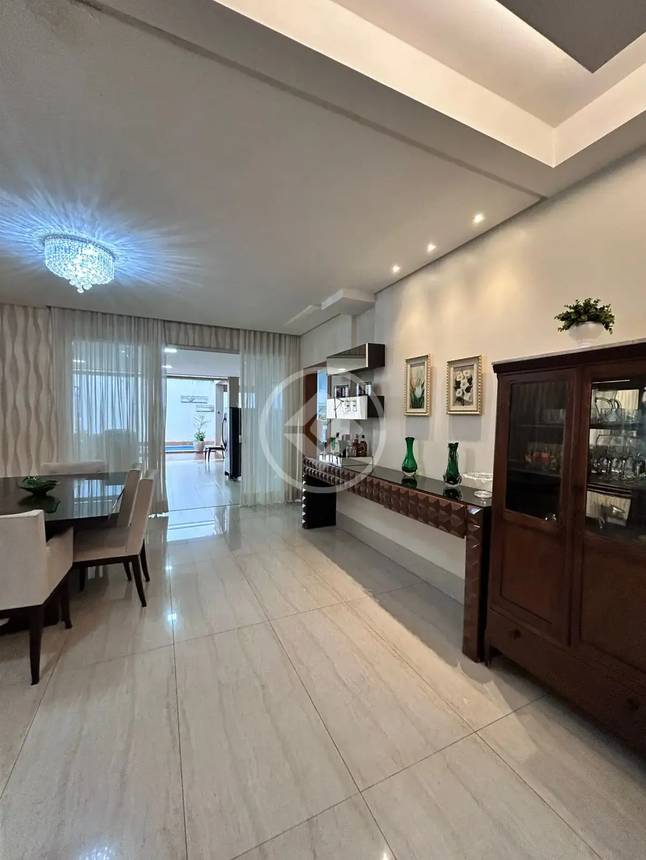 Sala de estar com mesa, cadeiras e luminária, além de iluminação embutida e piso de madeira